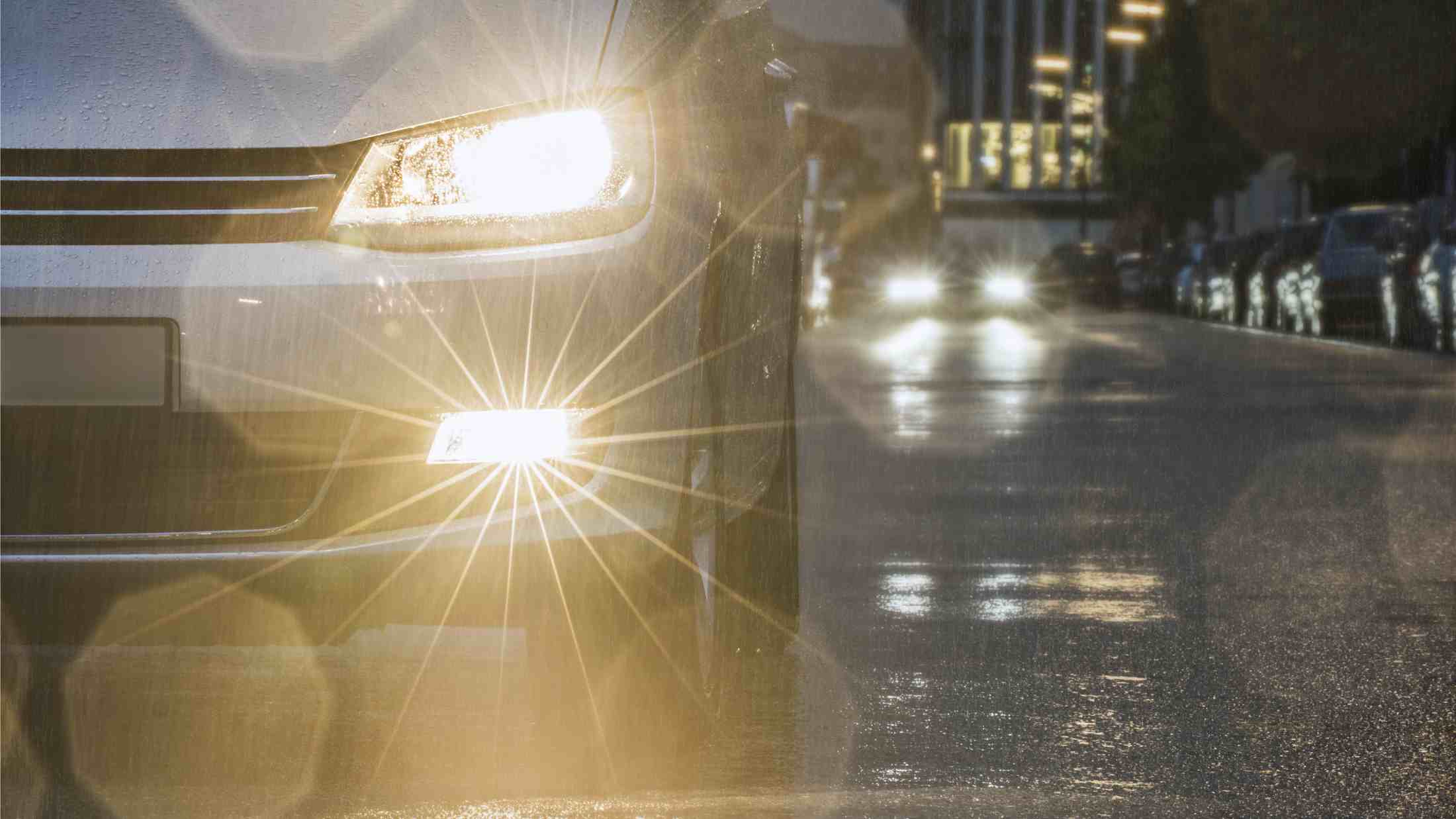 Car driving down urban street in rain