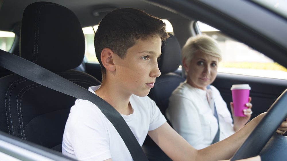 Focused teenager learning to drive a car with his mother in passenger seat holiday a coffee cup.jpg