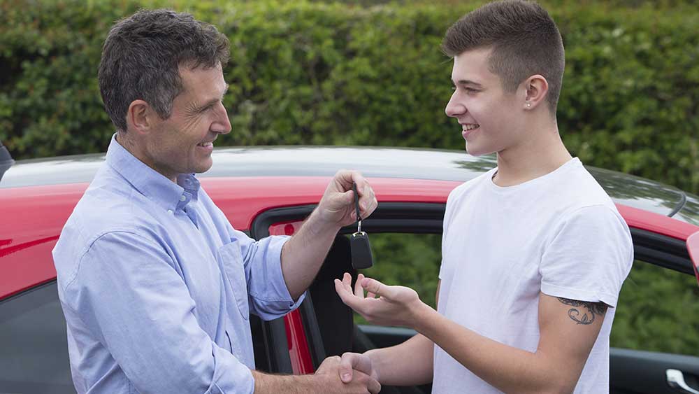 Man giving key to a teenager having sold his car to him