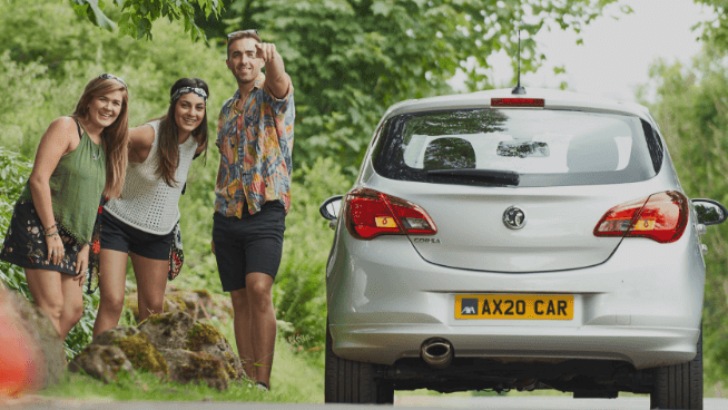 Two young women and a man stood by side of a silver car