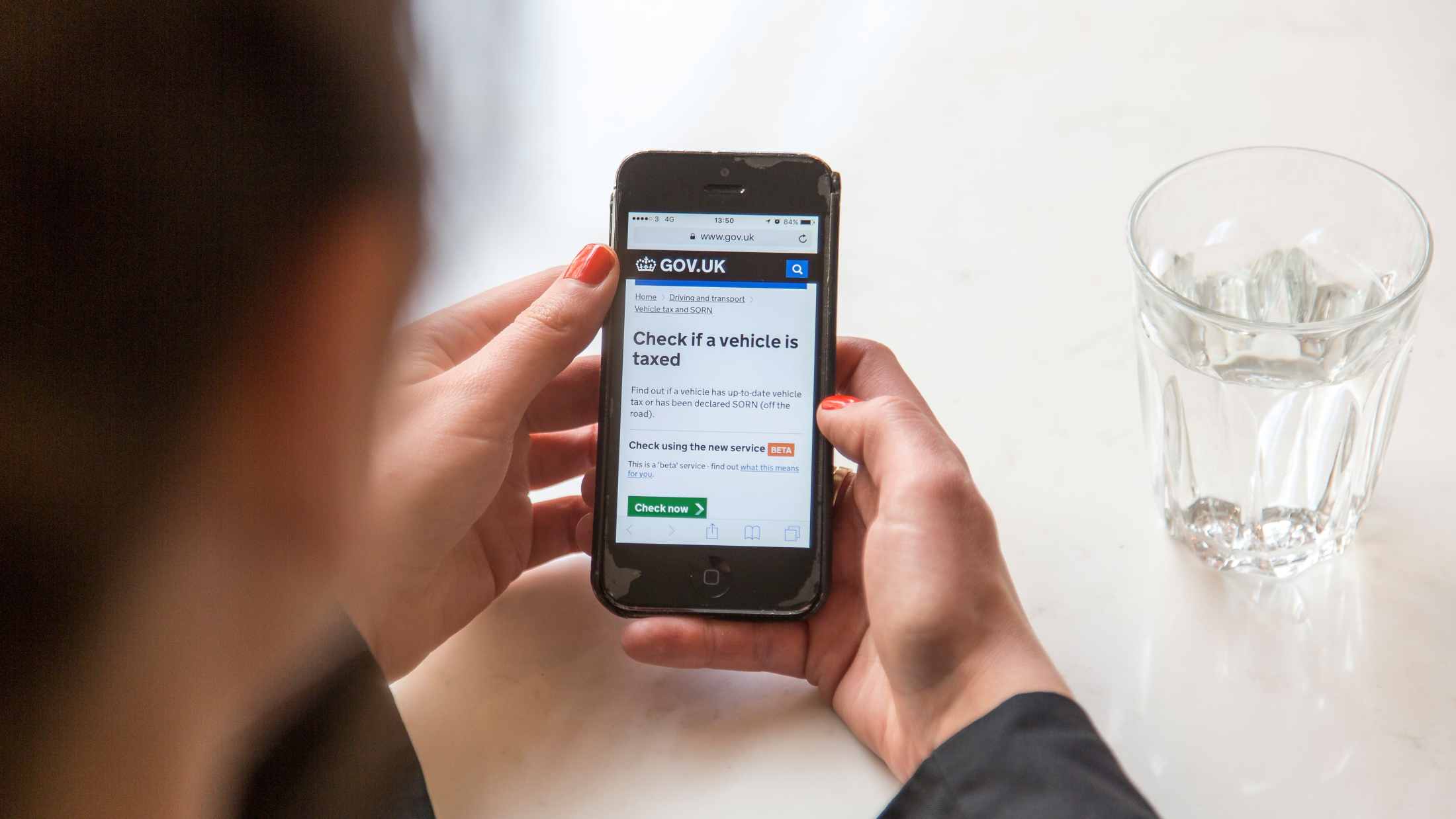 Woman holding an iPhone checking if her vehicle is taxed on the GOV UK website