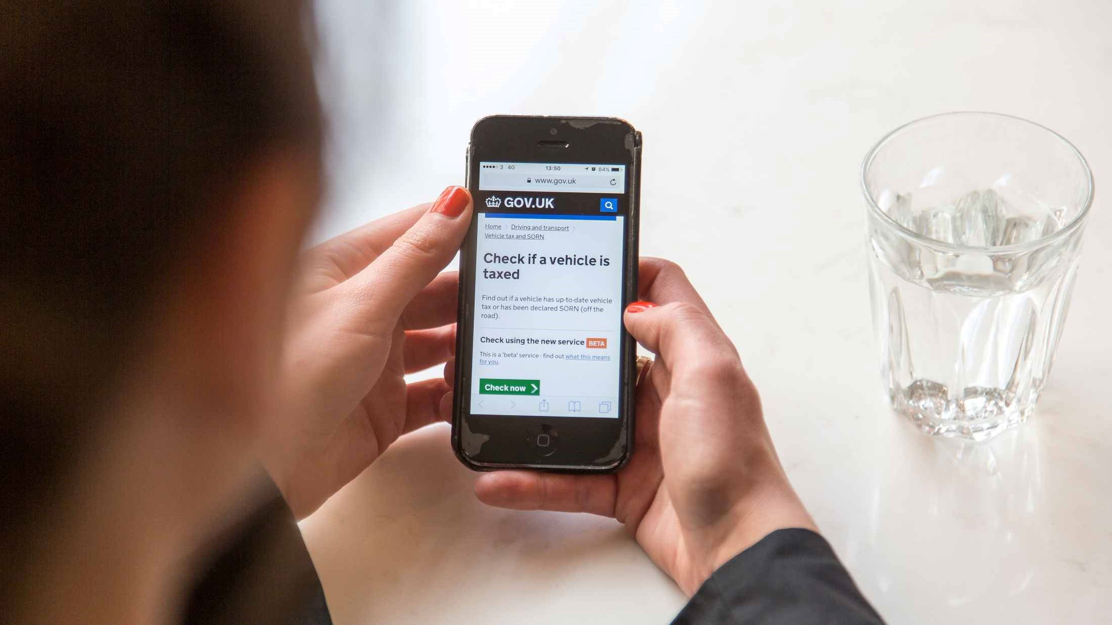 Woman holding an iPhone checking if her vehicle is taxed on the GOV UK website