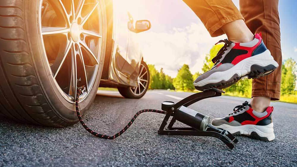 Woman wearing trainers using a foot pump to inflate a car's tyre