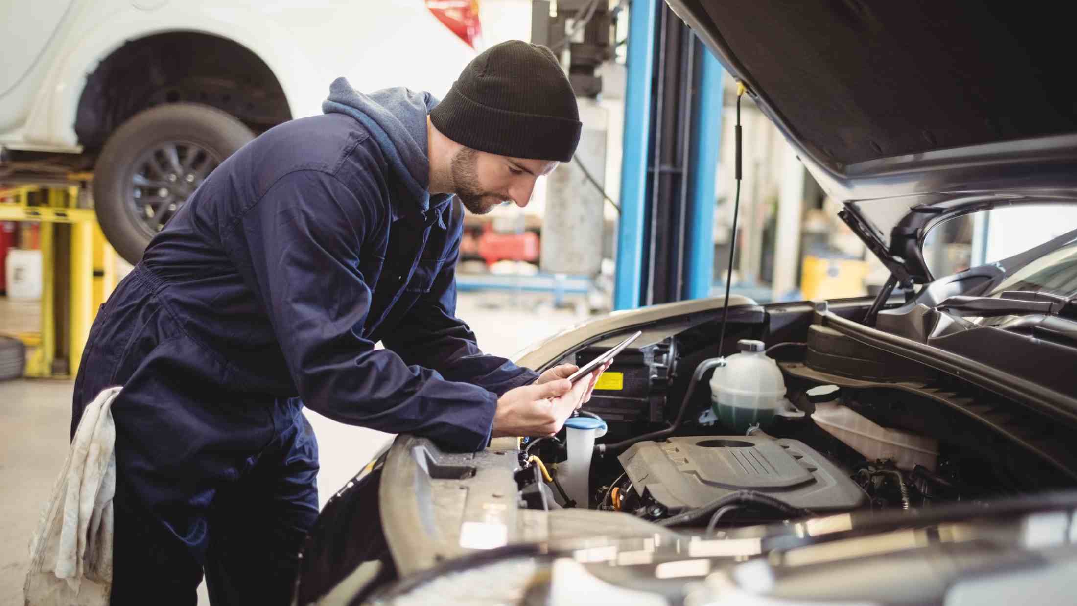 Young repairman working on a car with a tablet
