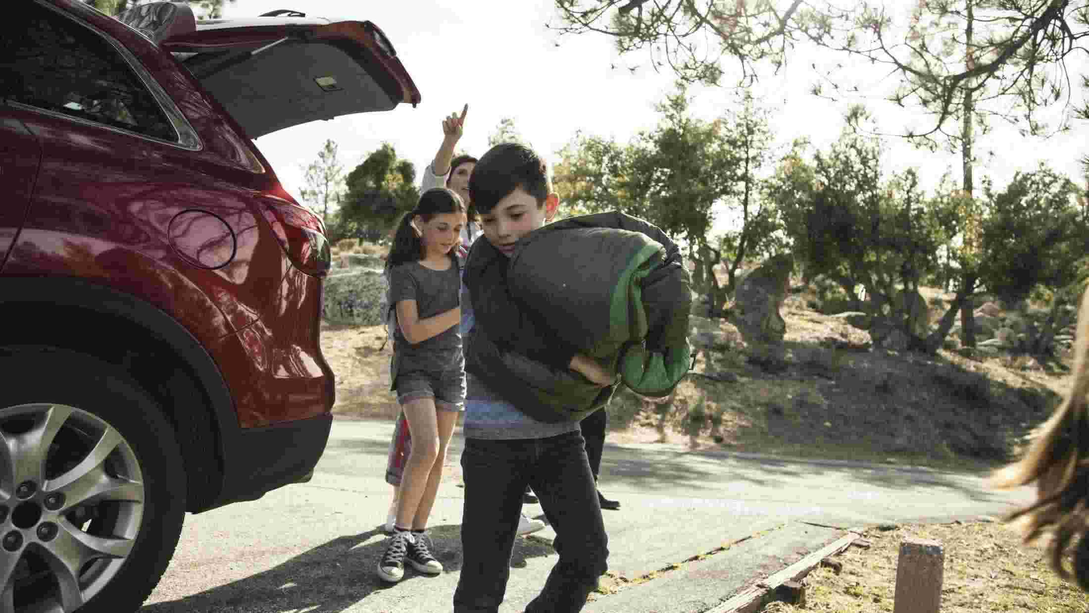 Young boy carrying a sleeping bag as his mum and sister close the boot of their car
