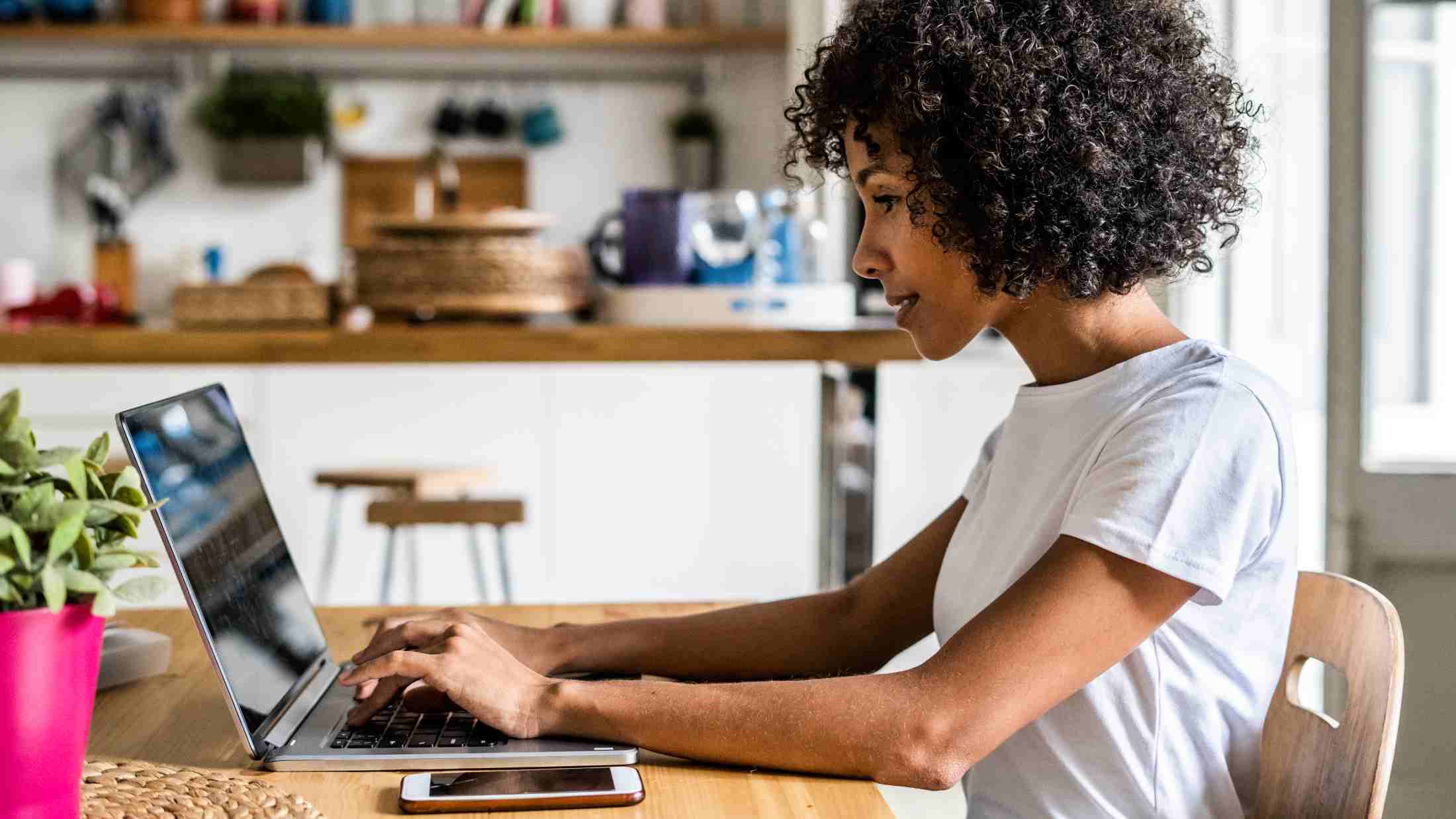 Black woman on her laptop while sat in her kitchen