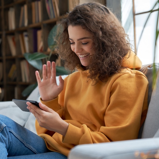 happy young girl sit on sofa at home holding phone looking at screen