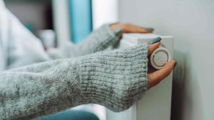 Cropped female hands in warm sweater trying to keep warm near battery radiator. Cold temperature