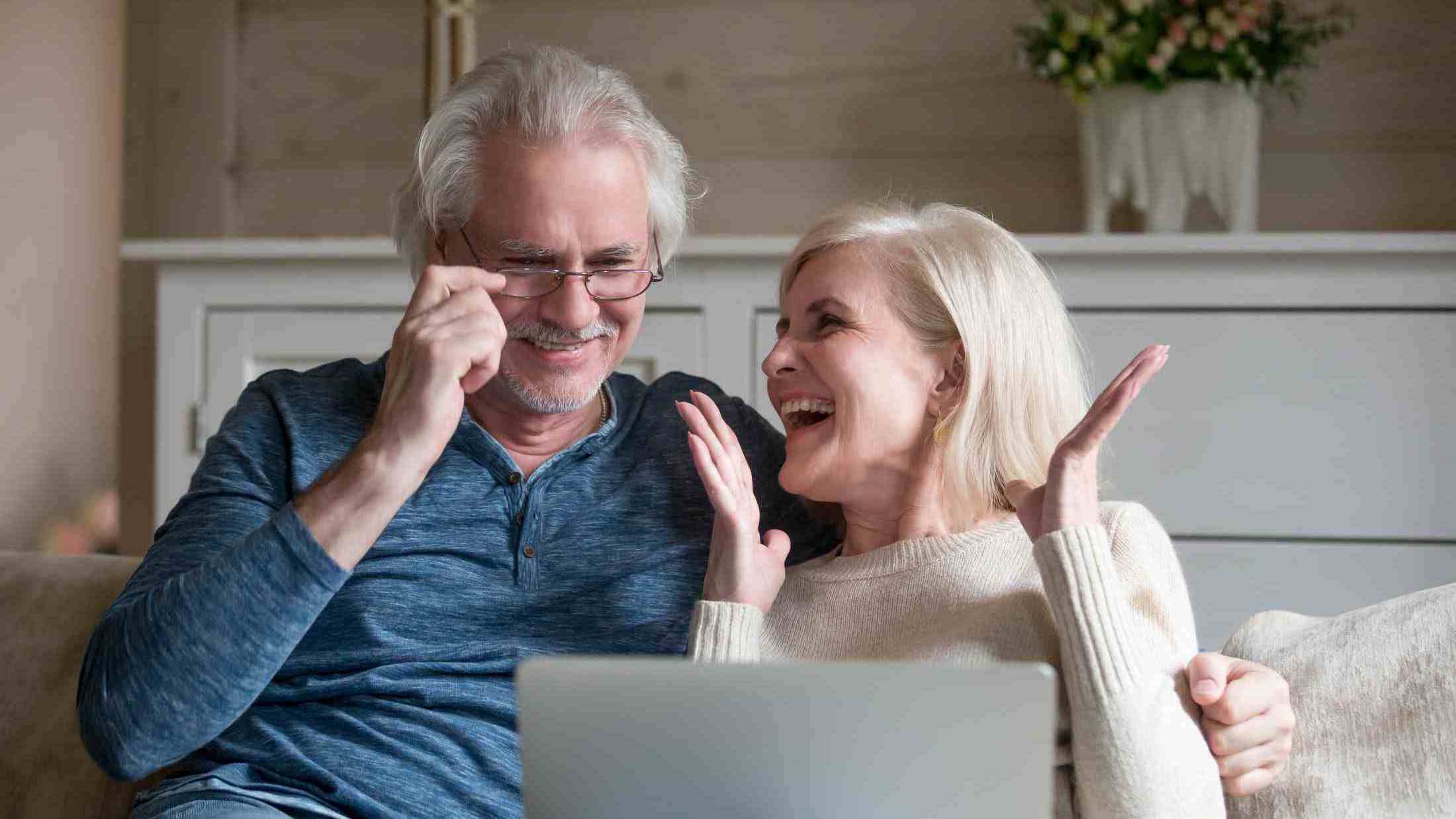 Happy senior couple laughing in front of a laptop in their living room