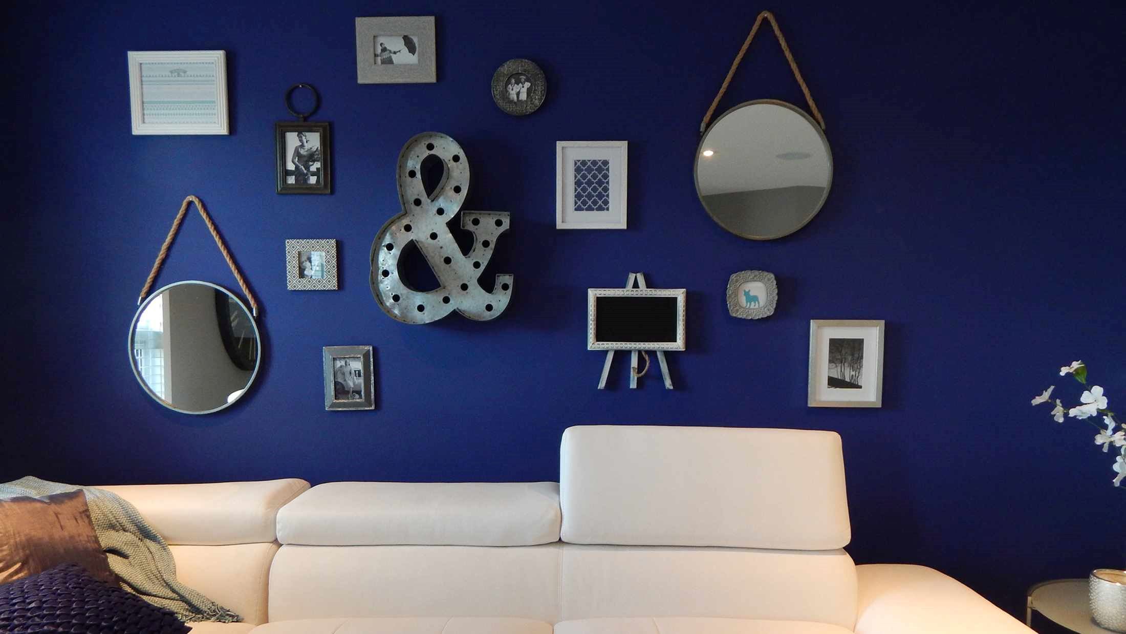 Leather sofa set near dark blue wall with hanging picture frames, mirrors and ornaments