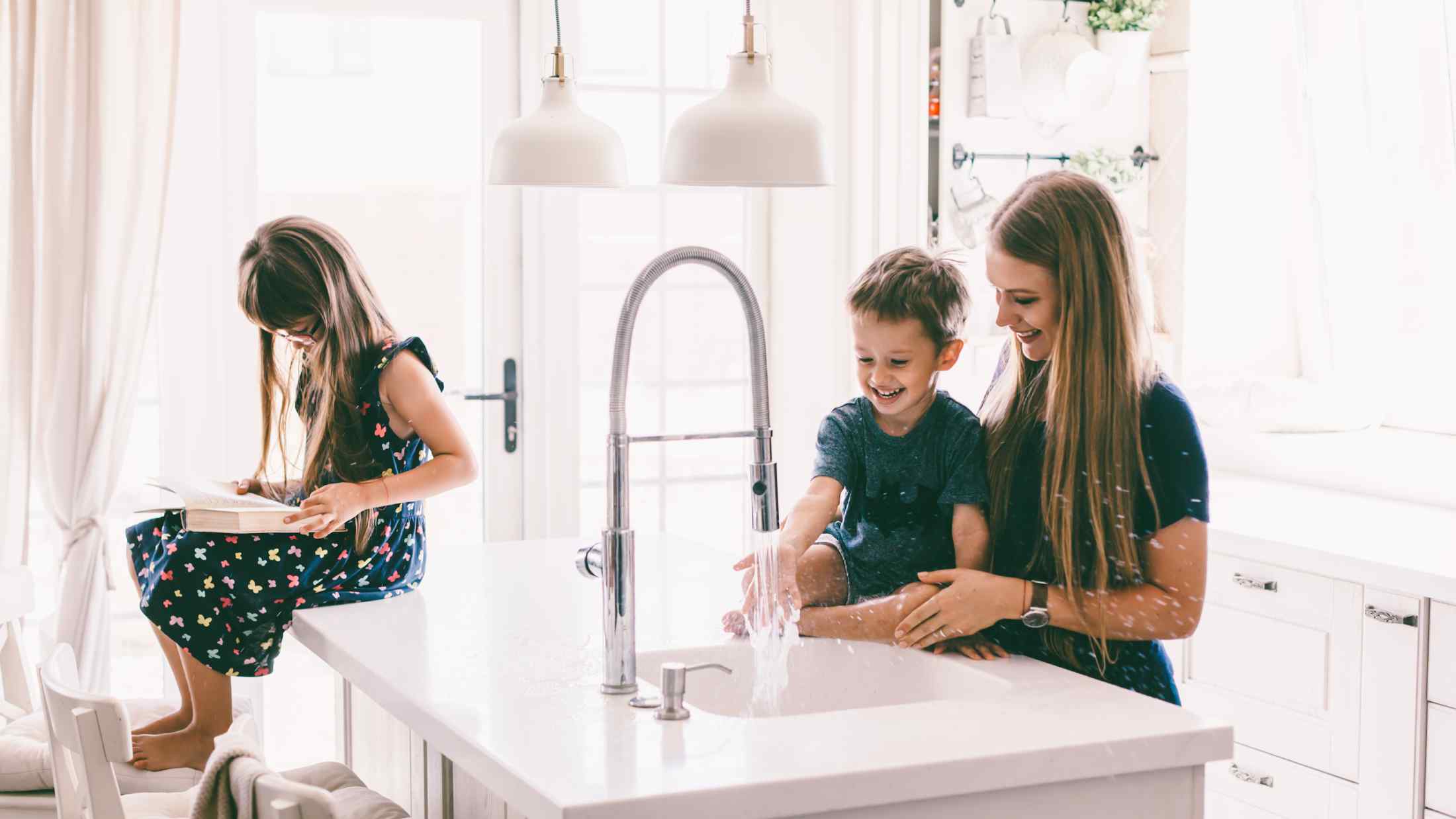 Mother with her children playing with water in kitchen sink at home