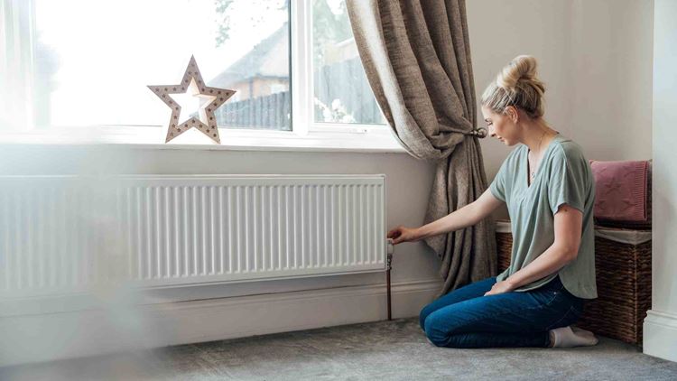 Side view of a young woman adjusting the thermostat on the radiator