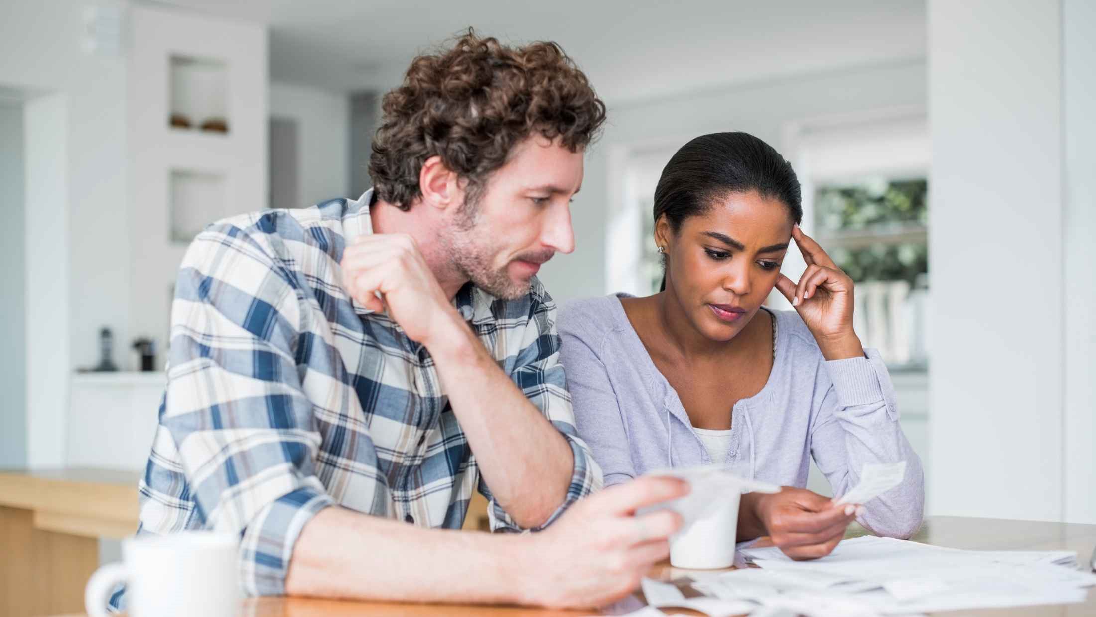 Tensed multi-ethnic couple reading bills at home