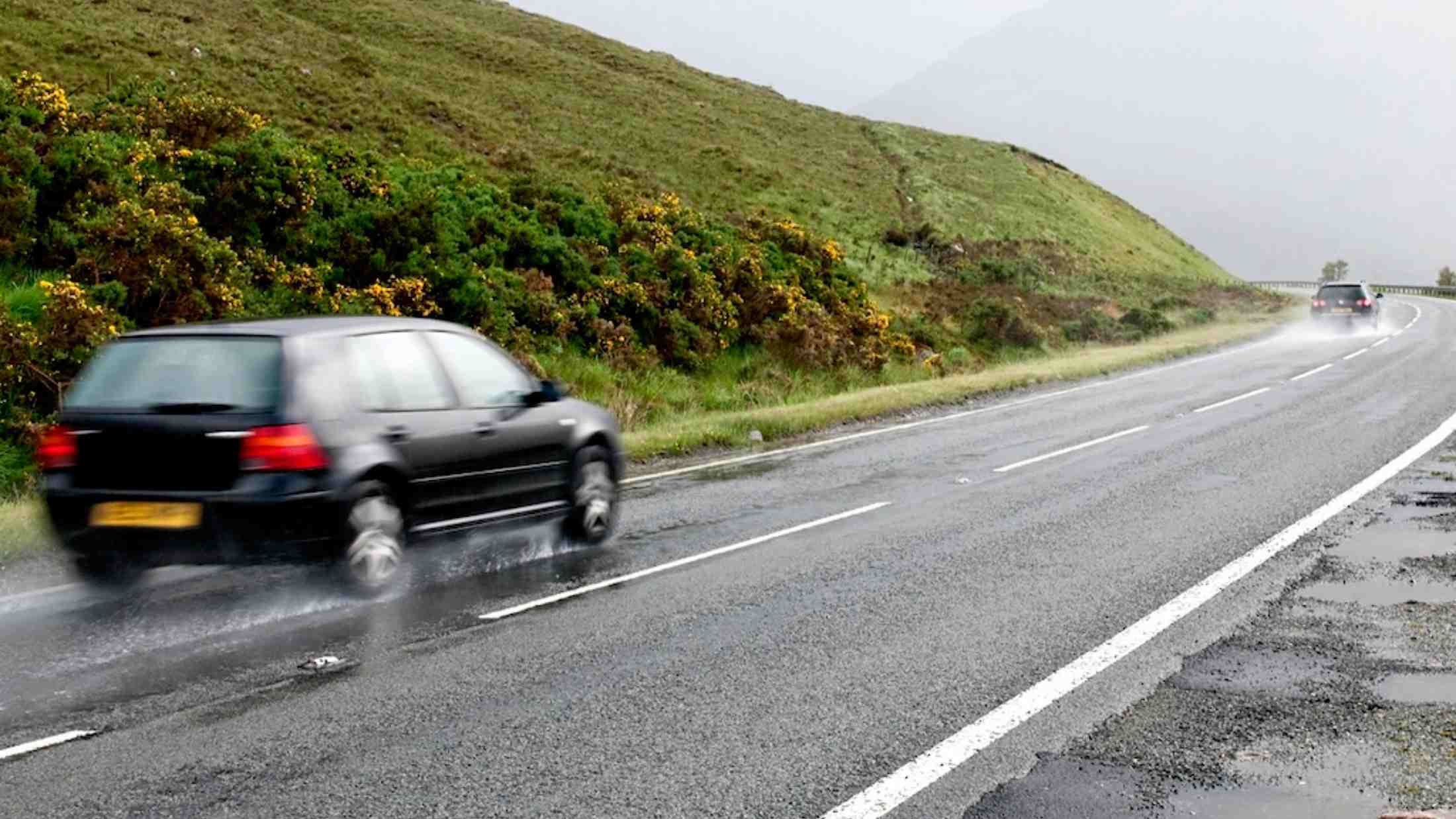 Two cars speed along a winding wet country road in Scotland