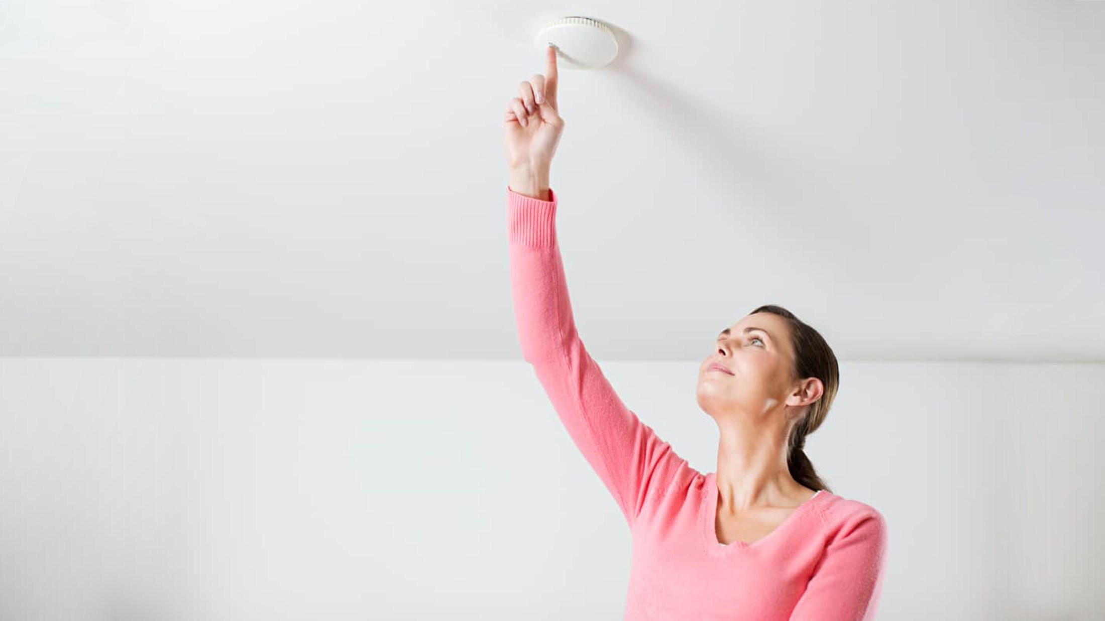 Young woman testing smoke alarm on ceiling