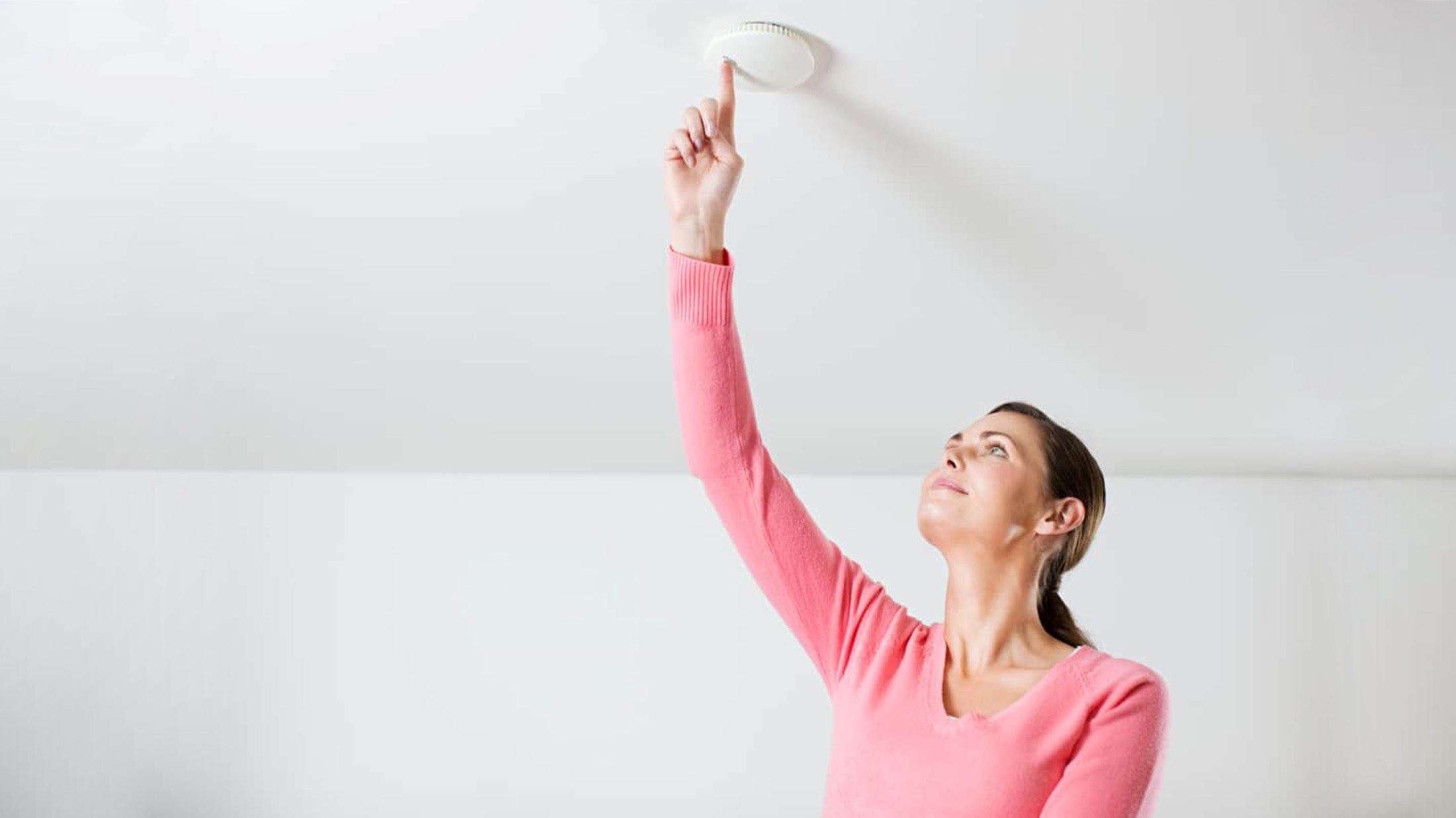 Young woman testing smoke alarm on ceiling