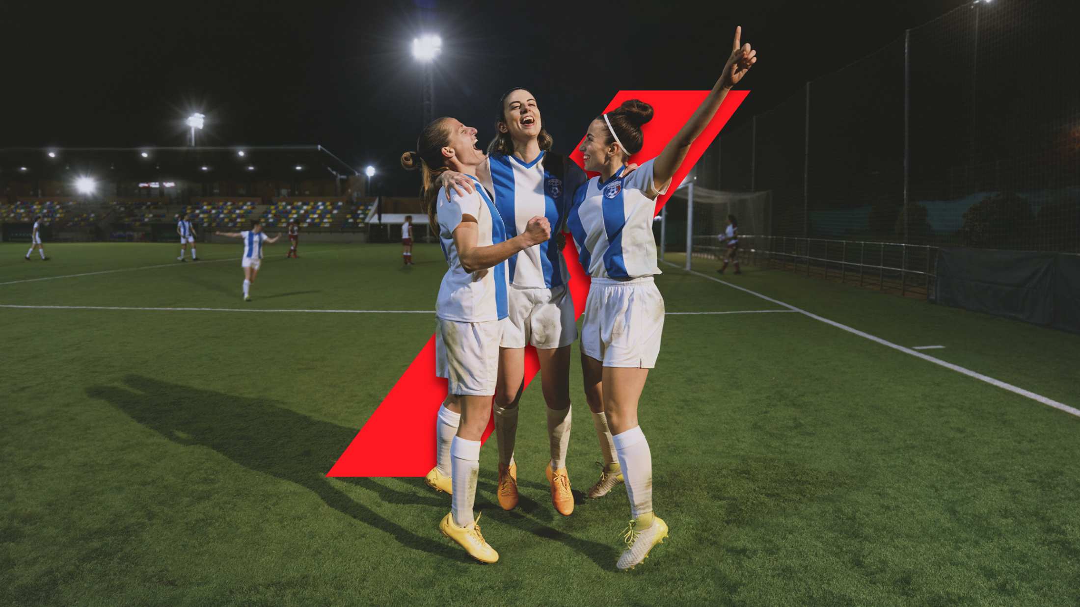 Three women celebrating a goal on the football field.