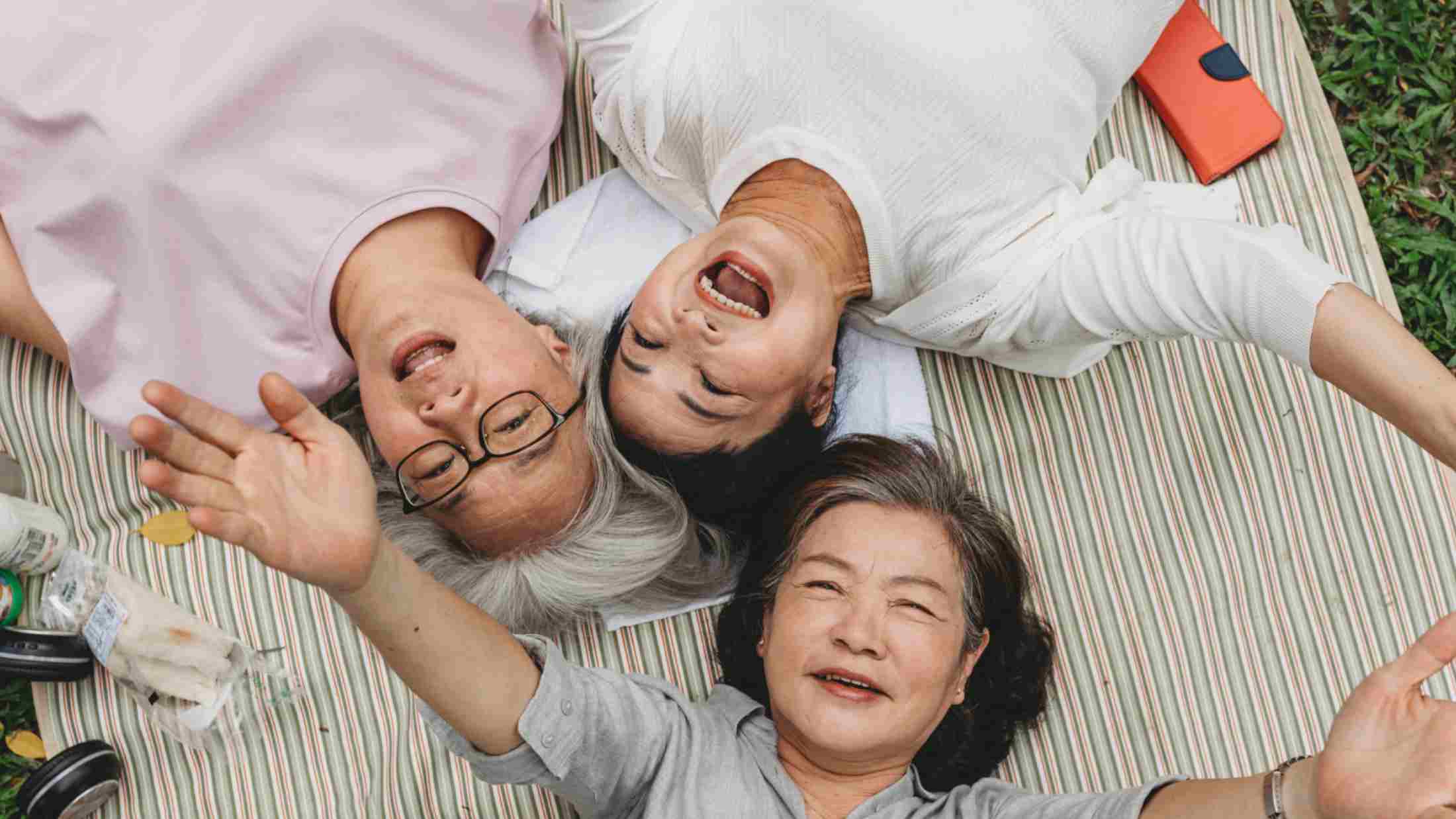 Three senior ladies lying down on the grass together