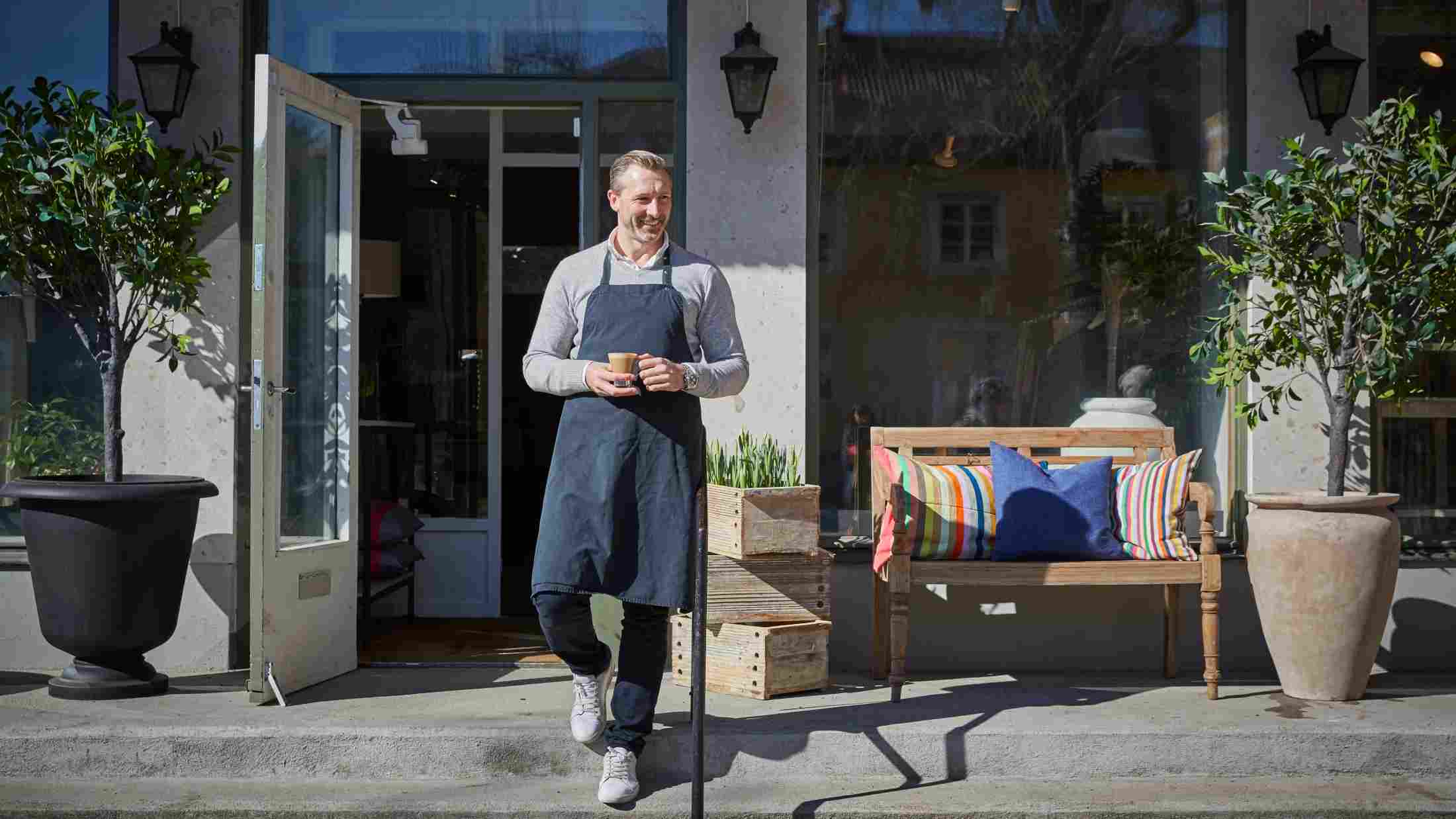 A handsome middle-aged owner holding coffee mug while moving down from steps outside his store