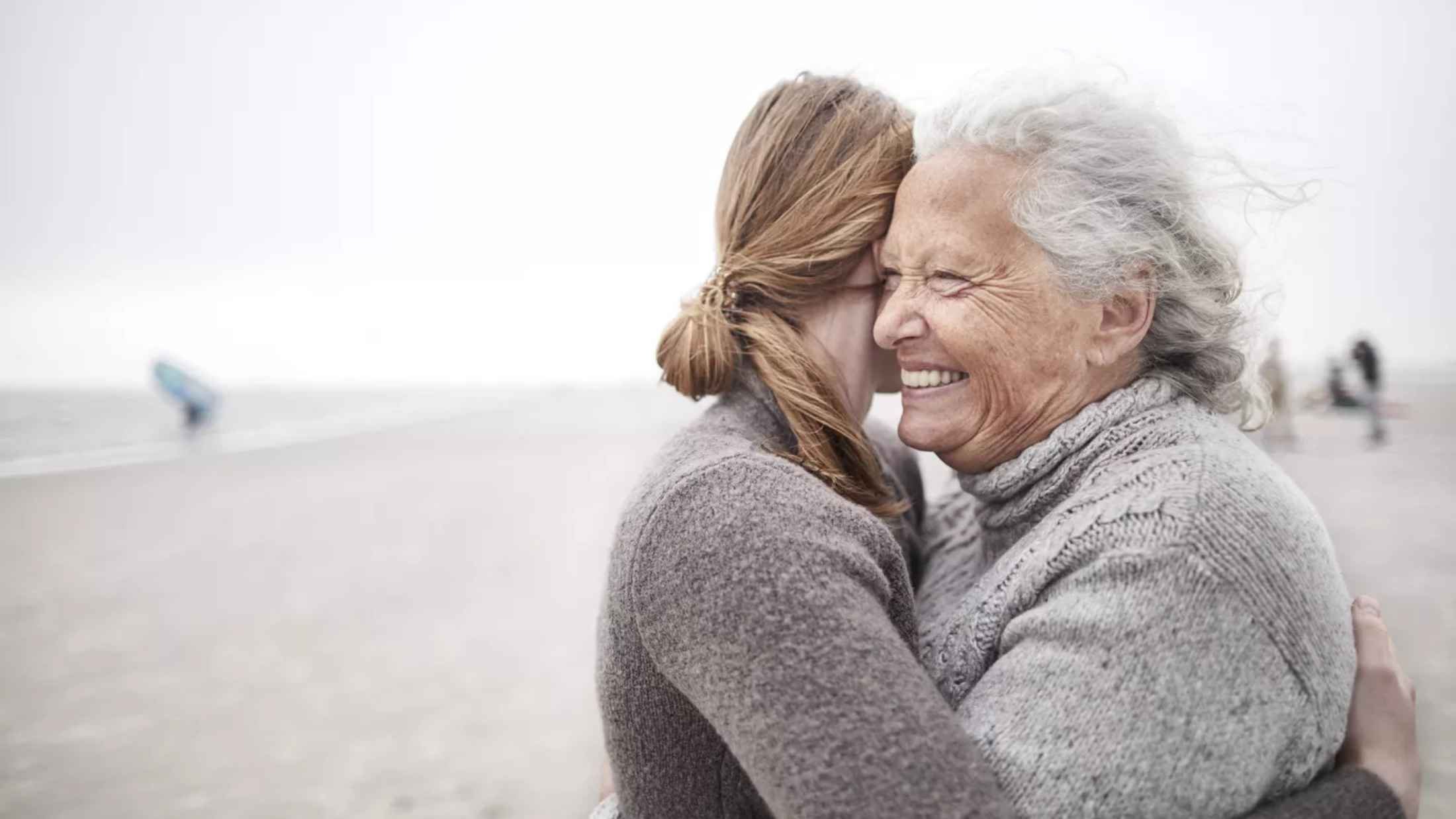Affectionate grandmother and granddaughter hugging on the beach