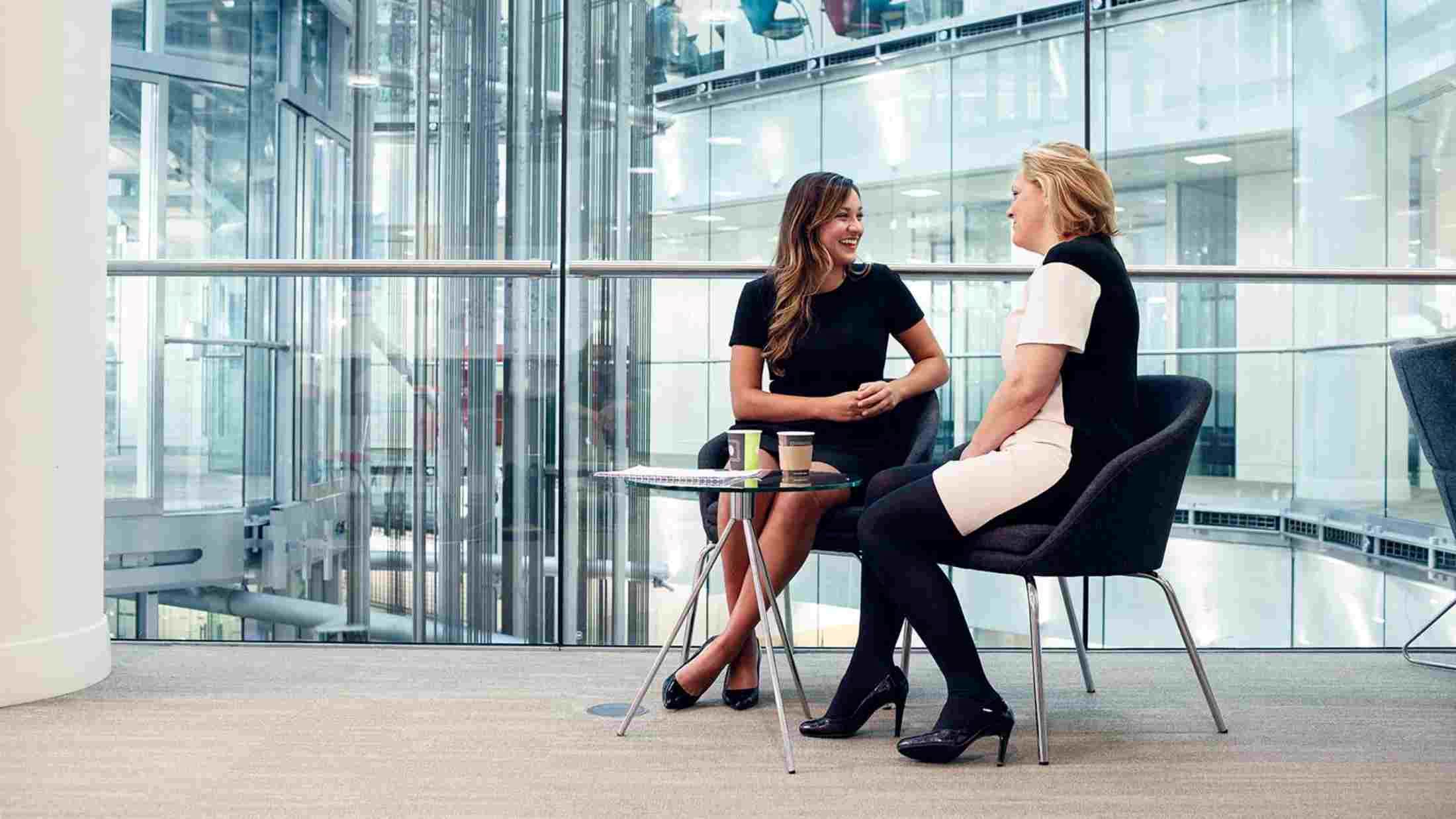 Two female colleagues have a conversation with in an open area of their