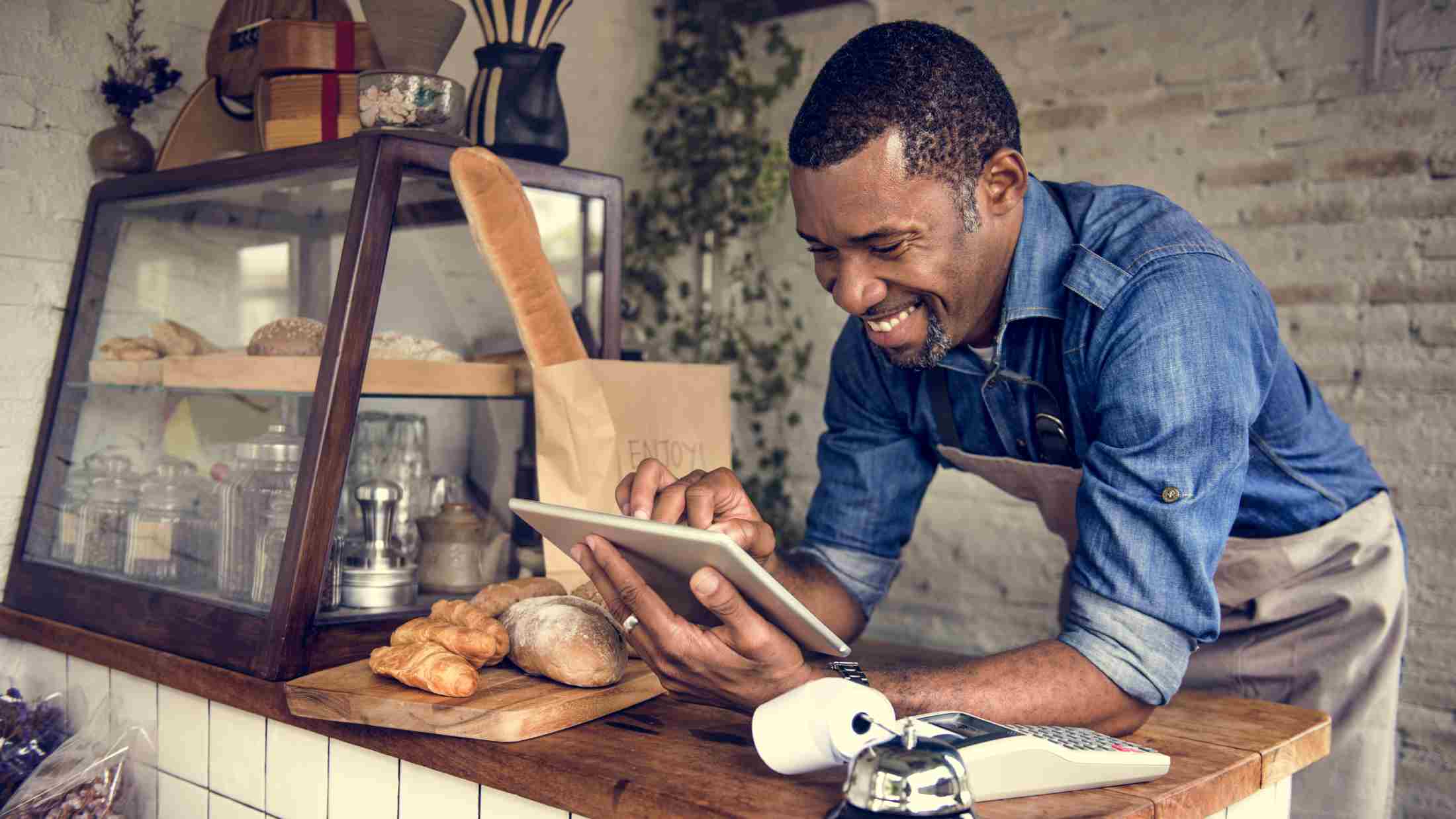 cheerful owner of a bakery shop is looking at his tablet at the cashier