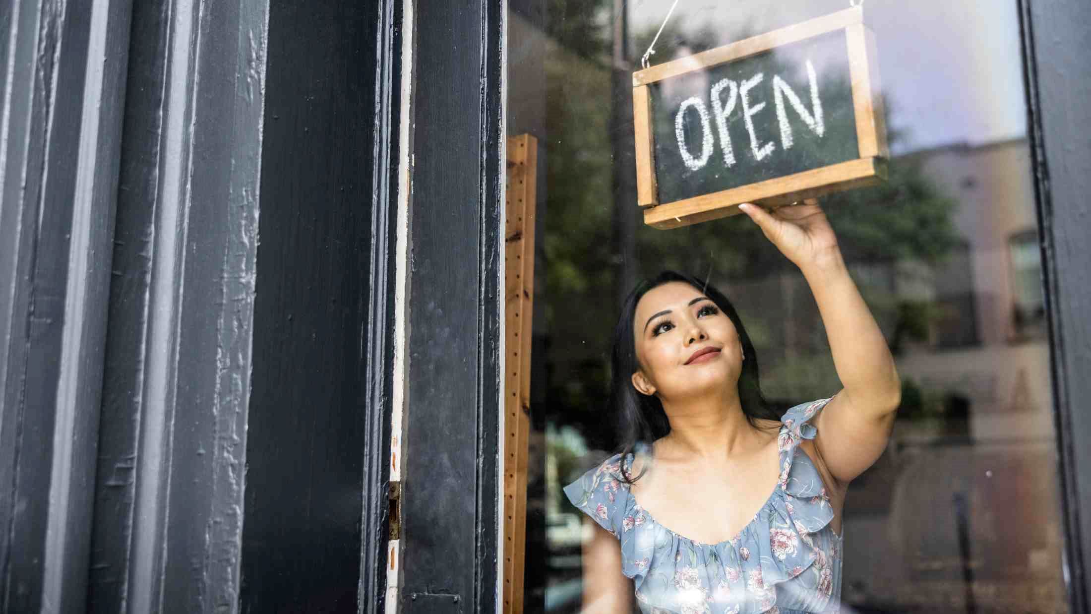 Female small business owner turning open sign in her store