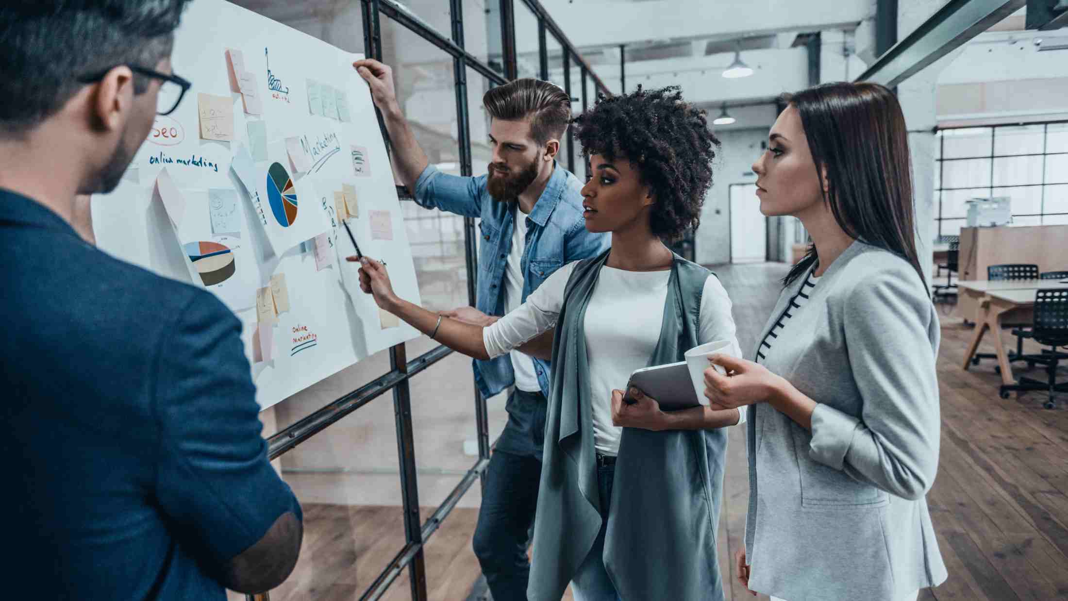Four young workers discussing business performance in front of a whiteboard