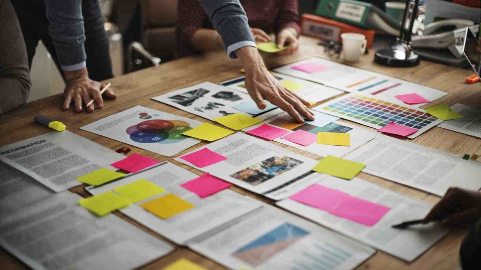 A team discussing a project around a table that has a lot of documents and sticky notes on it