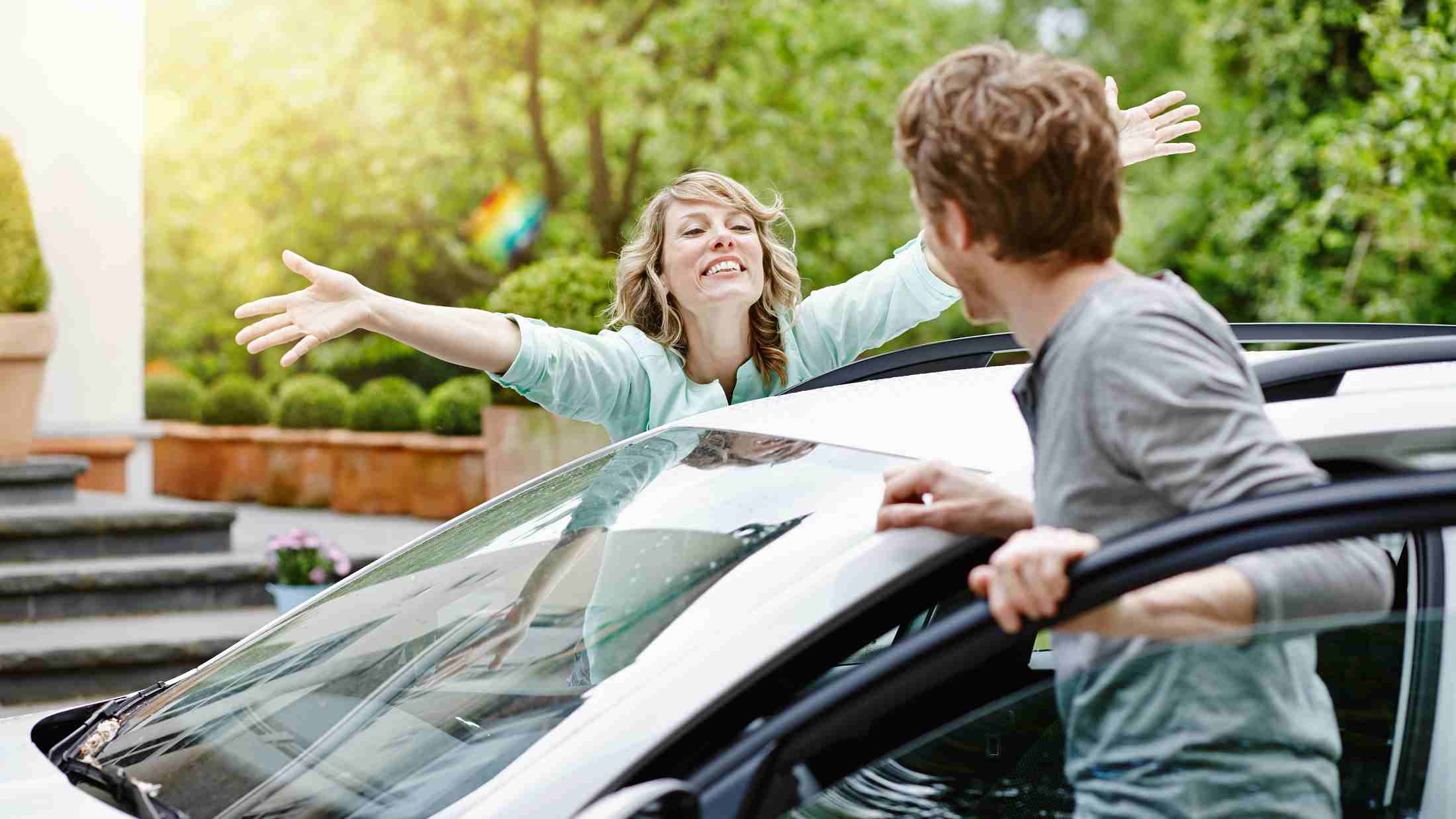 Happy woman with outstretched arms looking at a man who is entering a car