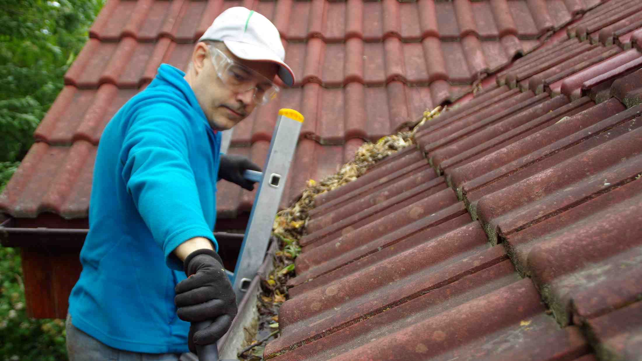 Man on ladder cleans gutter on a house roof