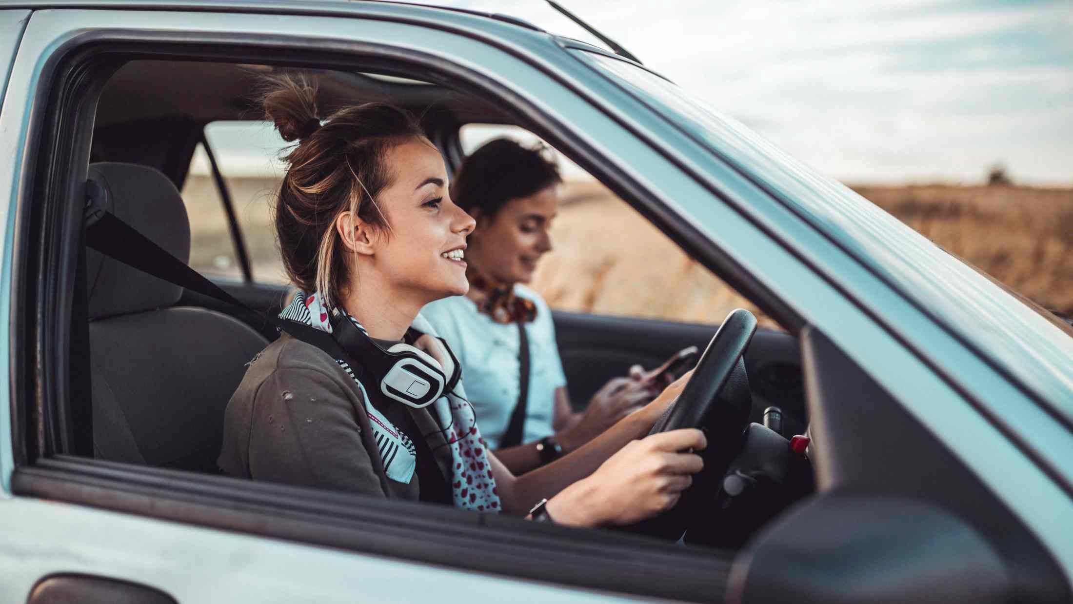 Two young women driving a car and enjoying summer road trip