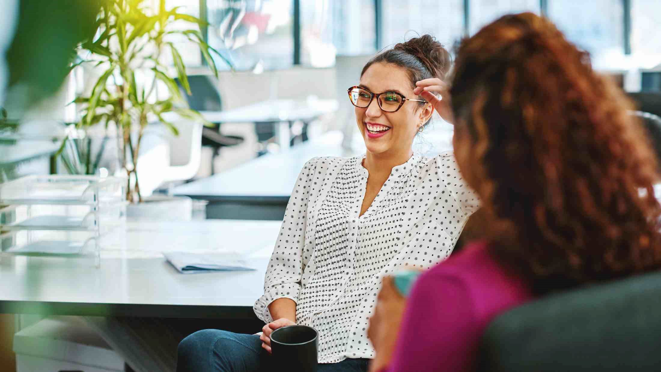 Woman holding a cup and laughing with her colleague