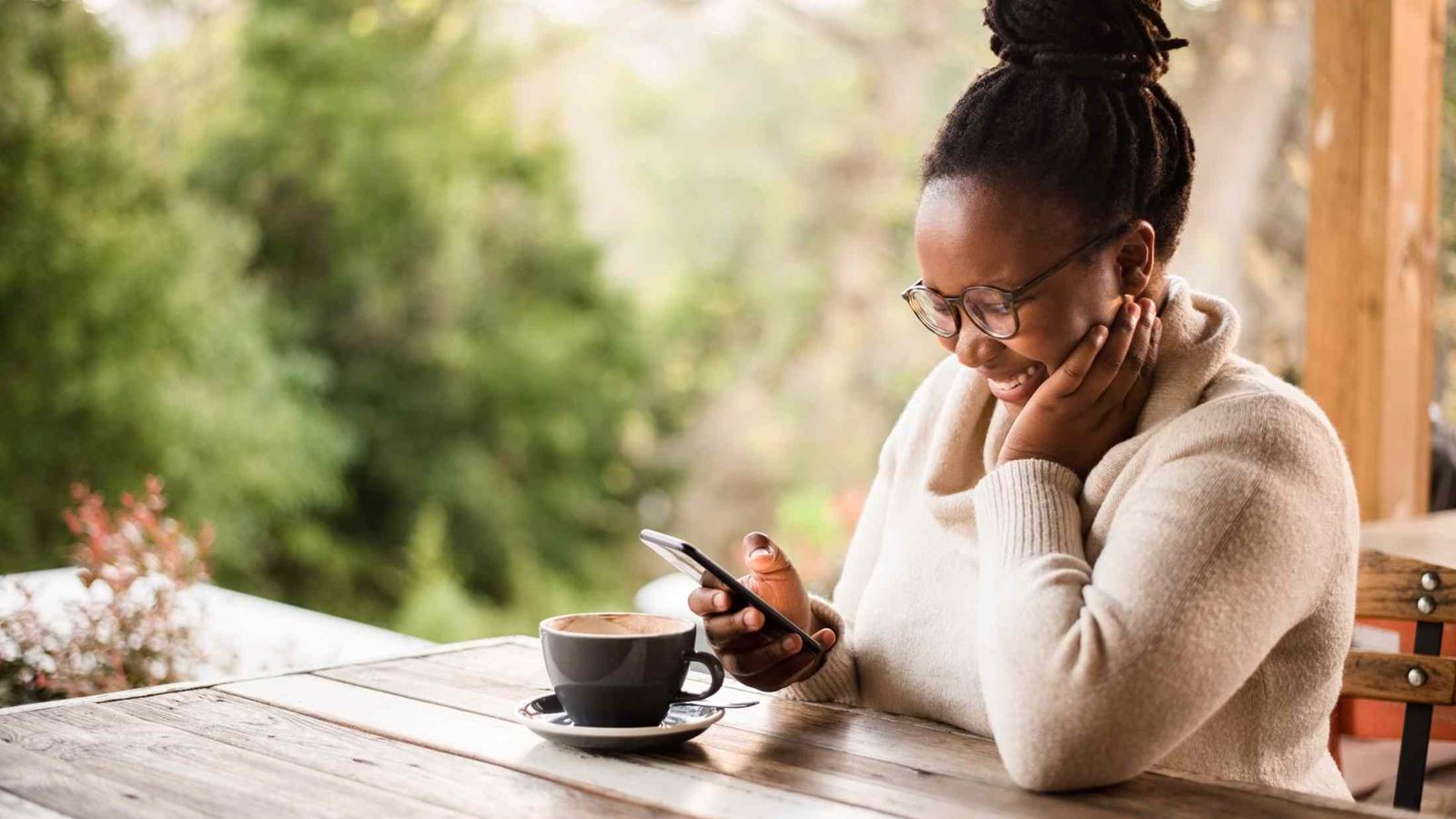 Young black woman reading message on mobile phone and smiling while sitting