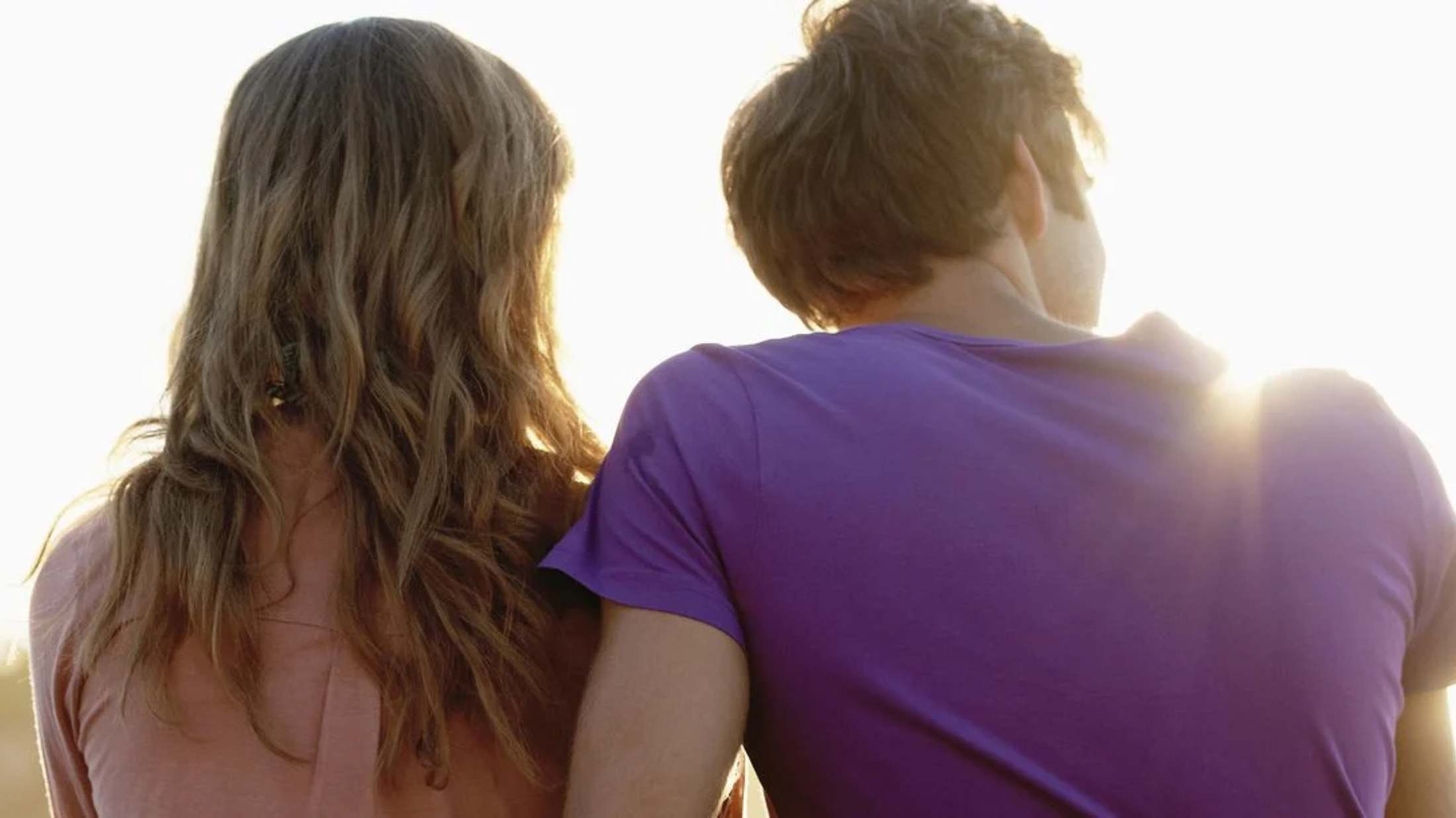 Back shot of a male and  a female sitting on a mountain sunset