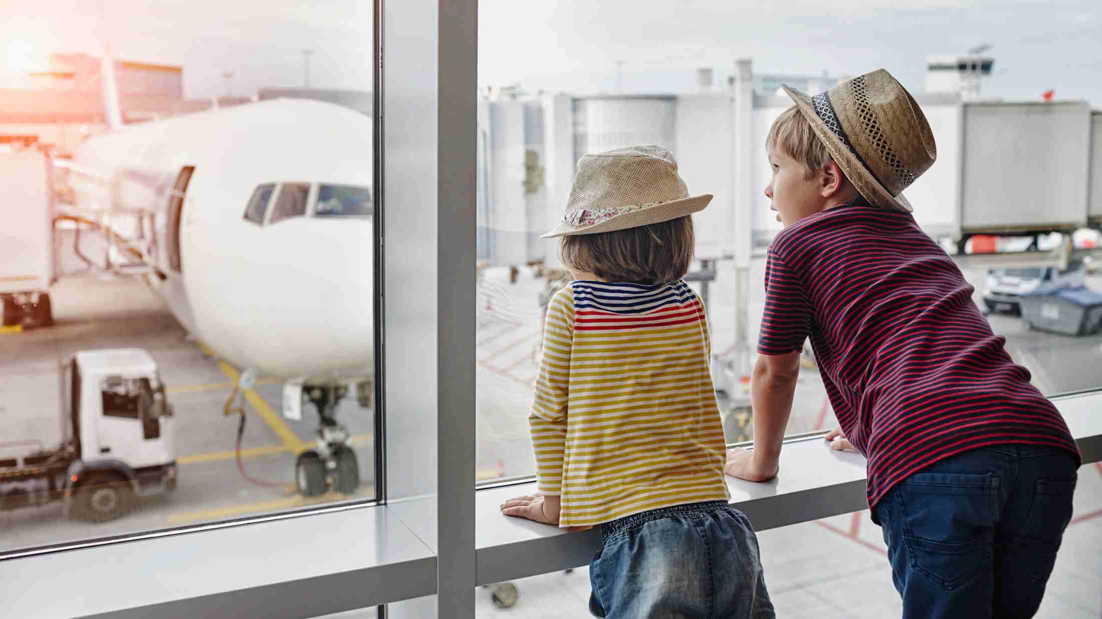 Two children wearing straw hats looking through window to airplane on the apron