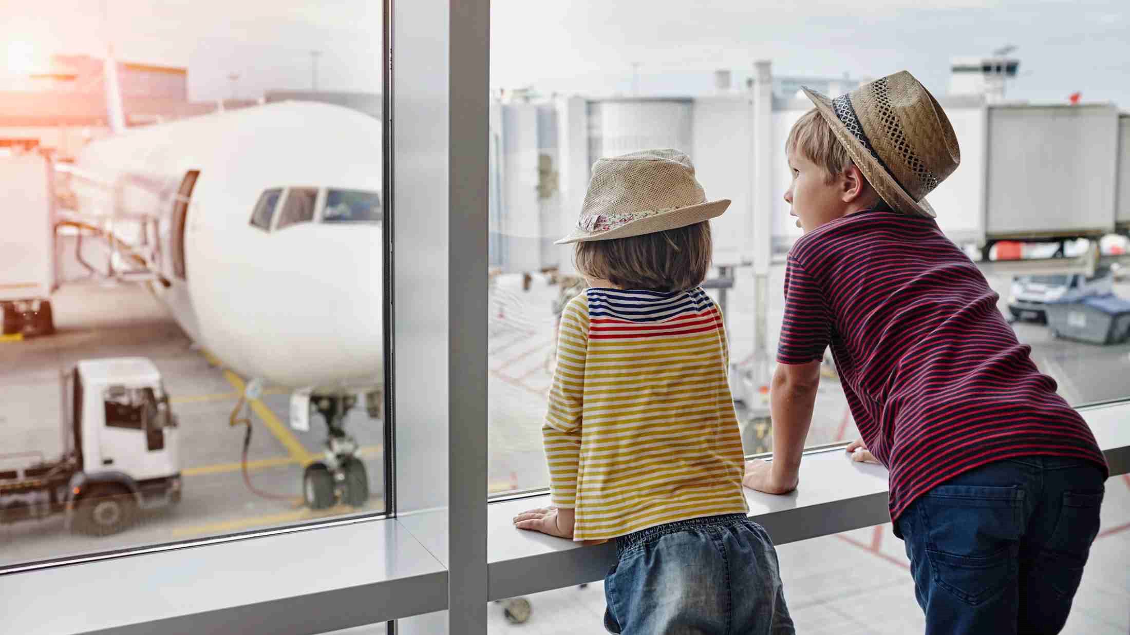 Two children wearing straw hats looking through window to airplane on the apron