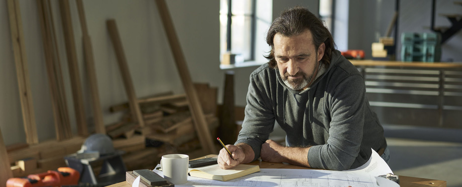 male tradesperson studying building planning drawings while on site